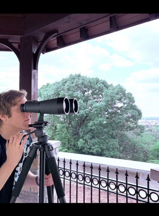 Man viewing through the Oberwerk 15x70 Deluxe, mounted on the Oberwerk 3000 Series tripod